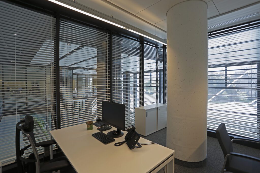 Realizacja żaluzji drewnianych w Eurocentrum Office Complex w Warszawie. Biuro ze szklanymi ścianami, na których zamontowane są żaluzje drewniane.